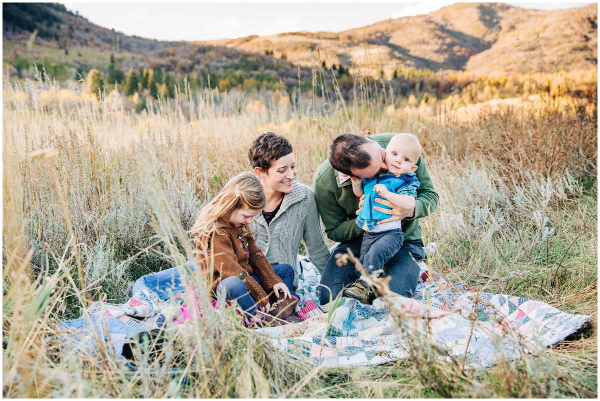 mom and dad playing with kids on a blanket in field