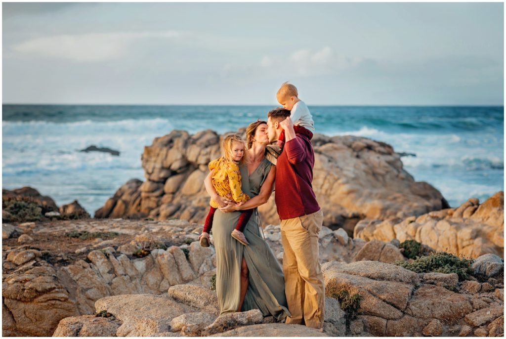 mom and dad kiss while holding kids at the beach