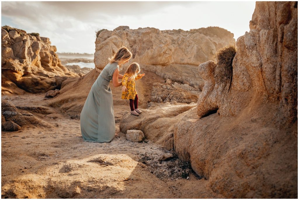 little girl climbing on rocks with mom holding her