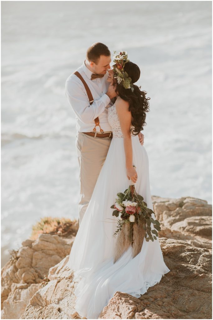 groom holding brides face and laughing by the ocean