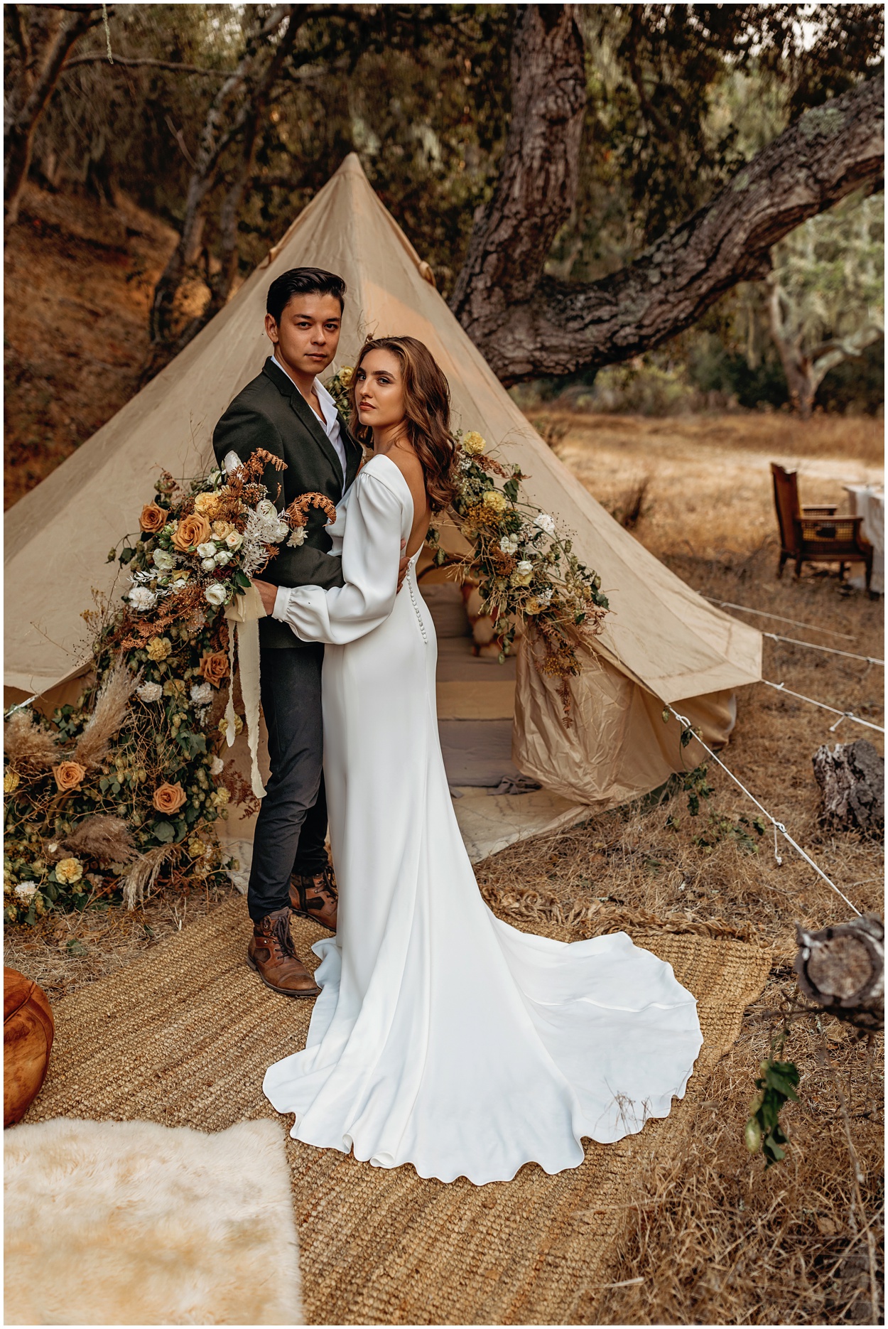 bride and groom by glamping tent and floral arrangement