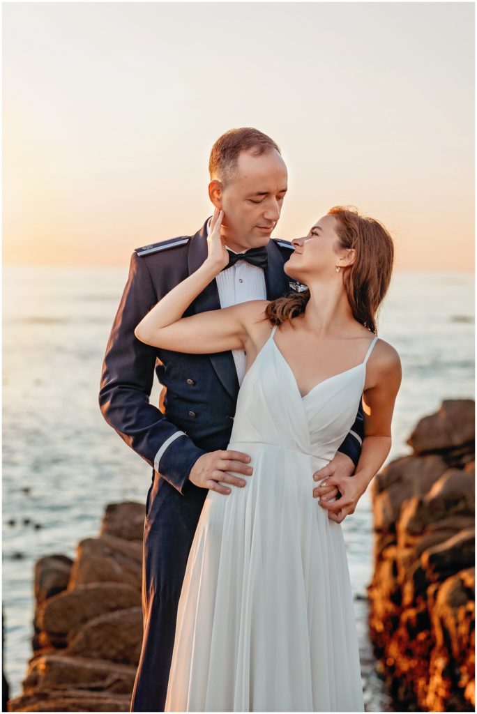 Bride gently touching her groom’s face as they embrace during their Carmel River Beach elopement at sunset, with soft golden coastal light behind them