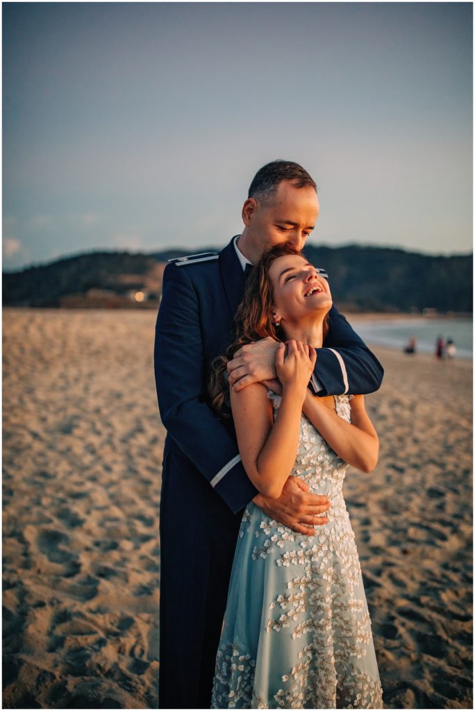 Groom embracing his laughing bride on the sand during their Carmel River Beach elopement, captured at golden hour with soft coastal light