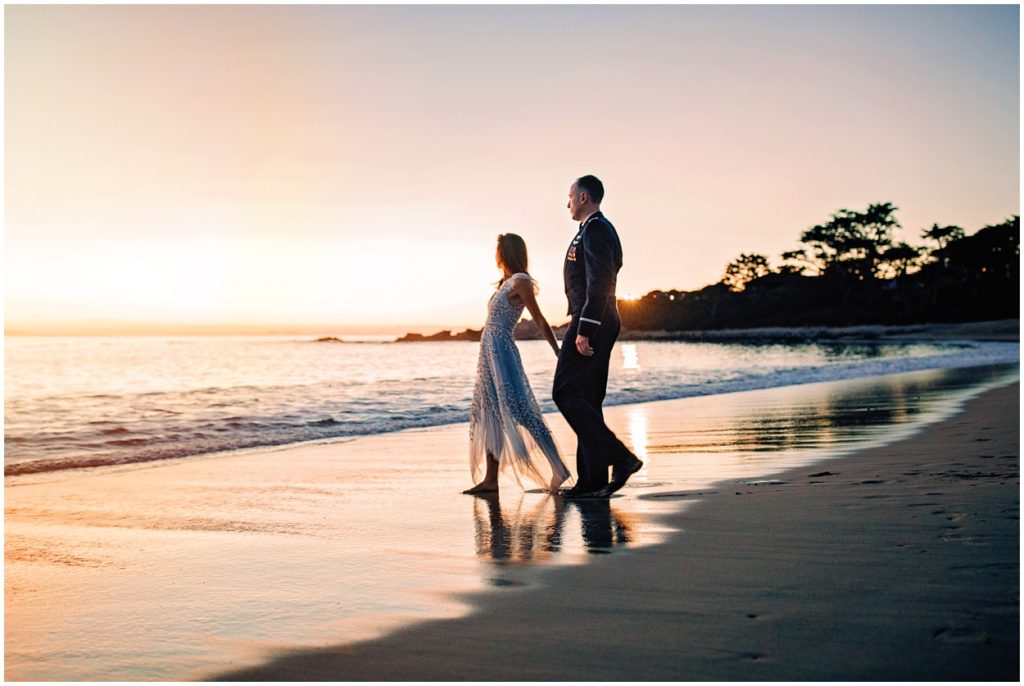 Bride and groom walking hand-in-hand along the water’s edge during their Carmel River Beach elopement at sunset, leaving soft footprints in the sand