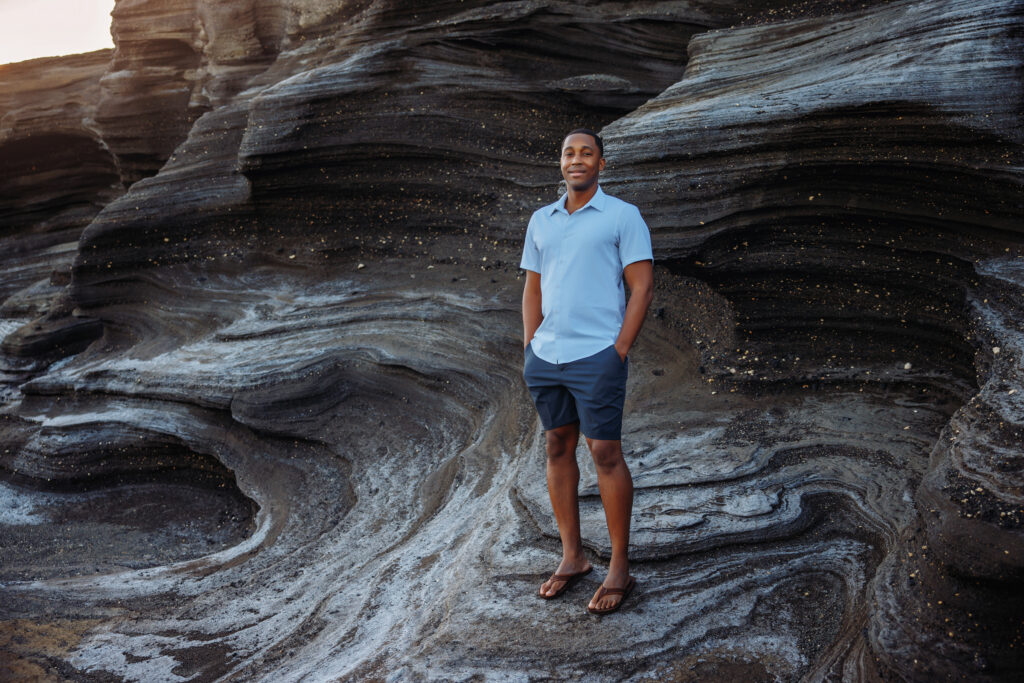 man standing on Hawaii rocks dressed in button down shirt and blues