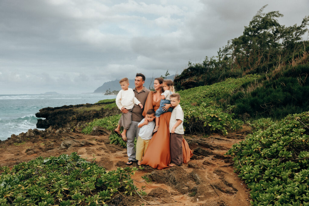 family standing on cliff at beach wearing warm color palate of rust, mustard, brown, cream and blue